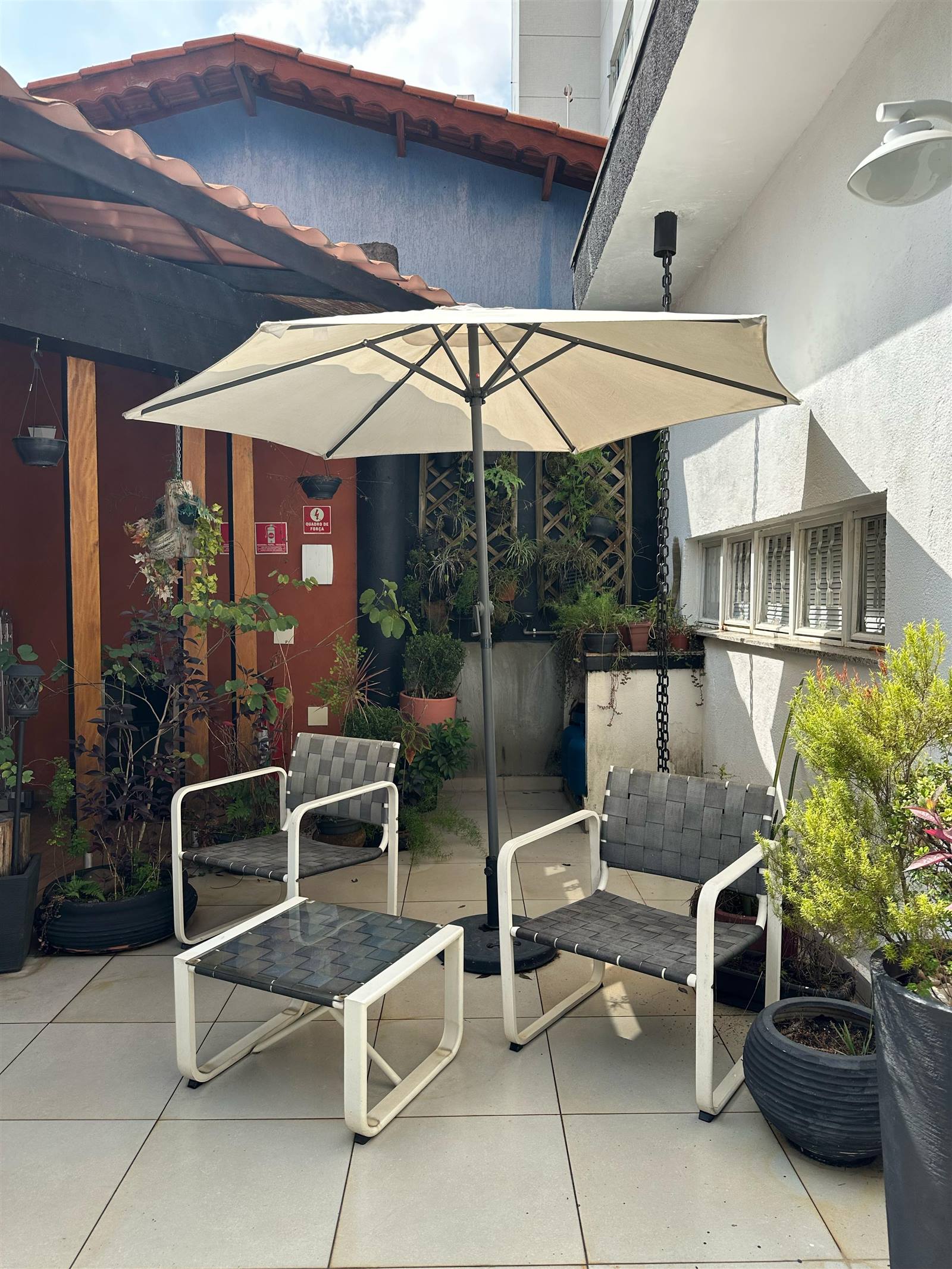 Área externa do Espaço Meneghelli com guarda-sol, poltronas e plantas durante o dia